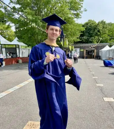 Alex Norcross celebrates graduating from Drexel: He is in cap and gown and is cheering/dancing/smiling.