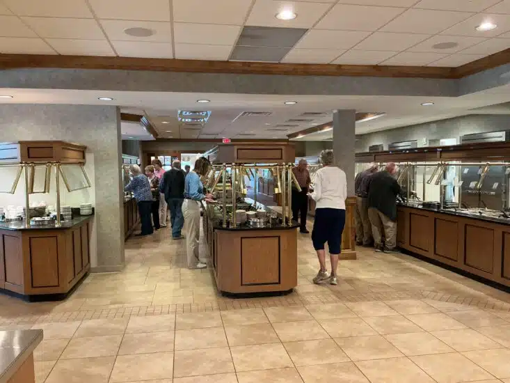 Buffet area at Bird-in-Hand Family Restaurant & Smorgasbord with guests selecting food from multiple serving stations in a bright, spacious dining room with wood and brass accents.