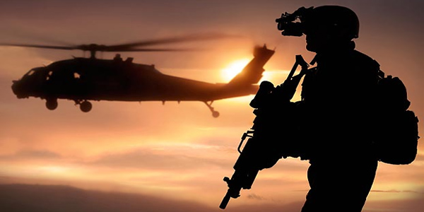 An armed soldier in silhouette with a helicopter hovering on his left.
