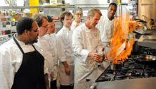 Group of men and women watching a chef prepare a food item