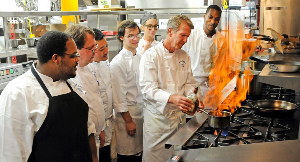 Group of men and women watching a chef prepare a food item