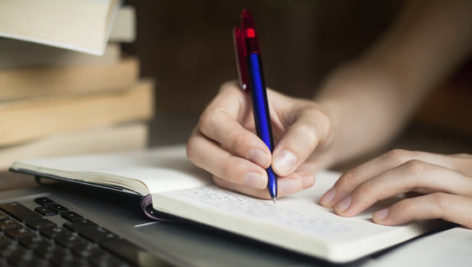 Someone's hand holding a pen writing in a journal.