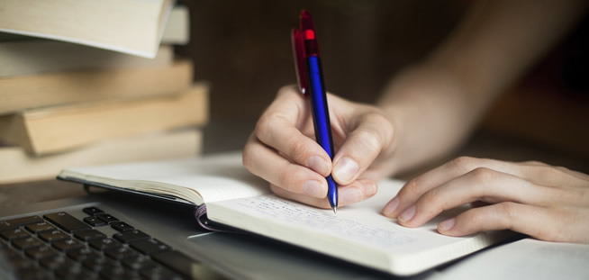 Someone's hand holding a pen writing in a journal.