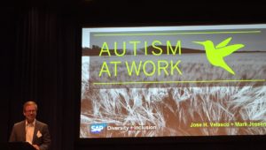 A man next to a screen giving a presentation on the Autism at Work program.