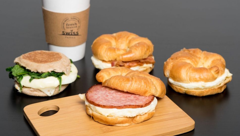 Four breakfast sandwiches on a sandwich board with coffee.