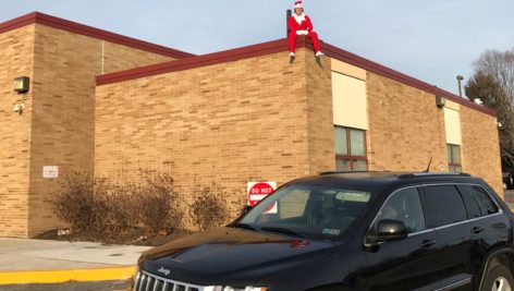 Aston Elementary School custodian Chris Farmer sits on the roof, dressed as Elf on the Shelf.