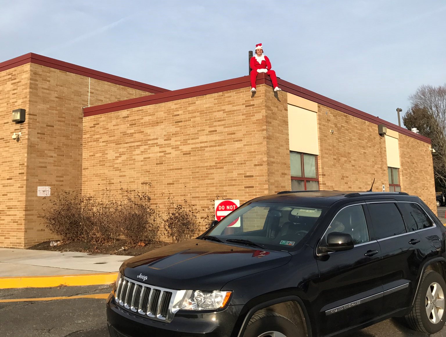 Aston Elementary School custodian Chris Farmer sits on the roof, dressed as Elf on the Shelf.