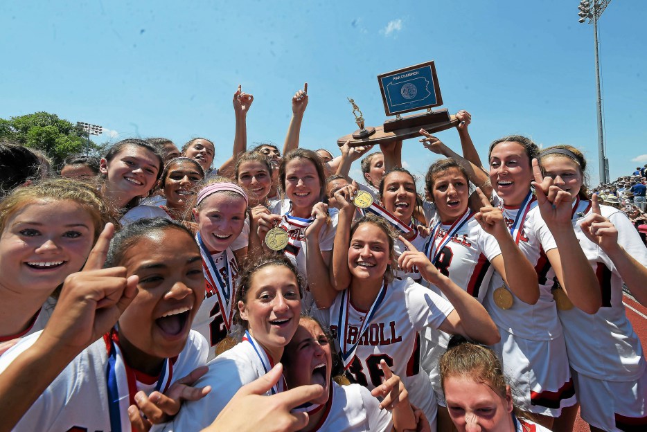Members of the Archbishop Carroll girls lacrosse team hold up a trophy in victory.
