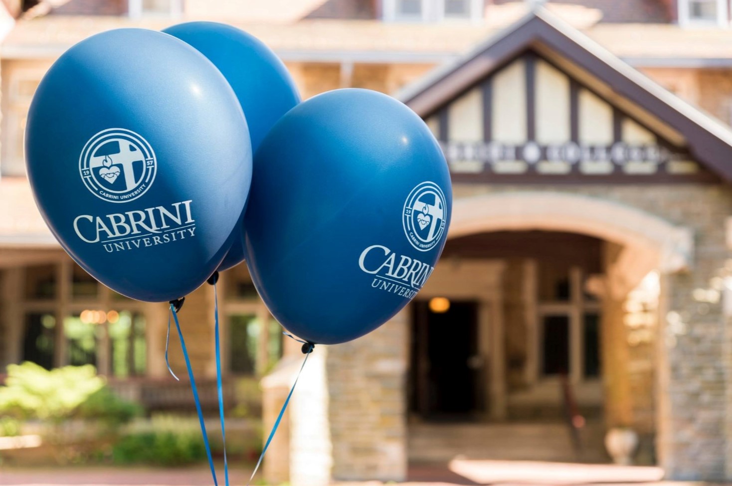 Balloons with the Cabrini University name and logo tethered to a building on campus.