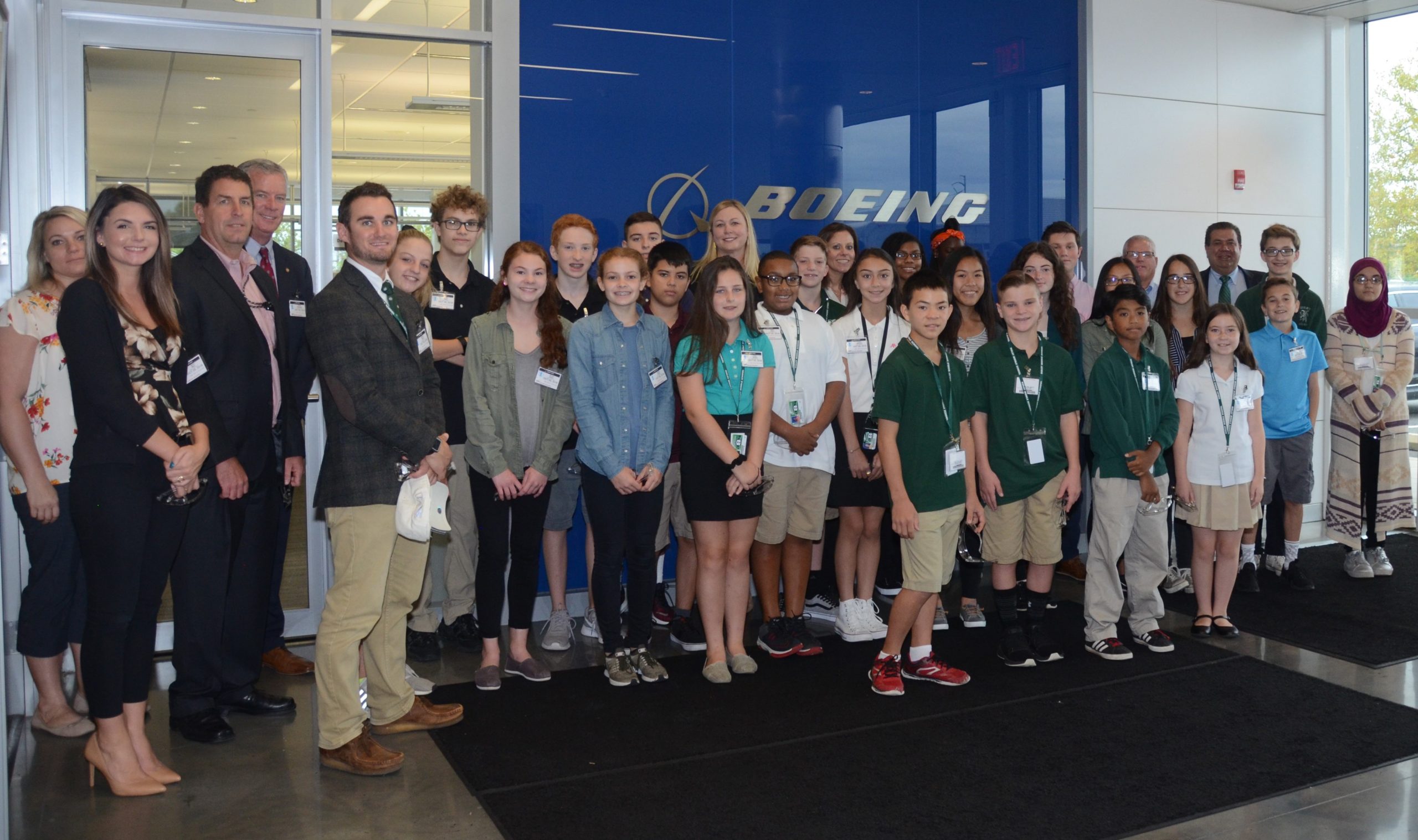 A group of adults and kids standing in front of a Boeing sign.