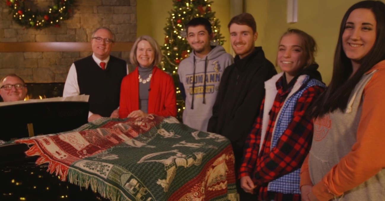 Men and women sitting together in a Christmas scene with a Christmas quilt.