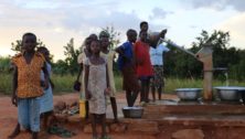 Residents of an African village wait for water at the well pump.