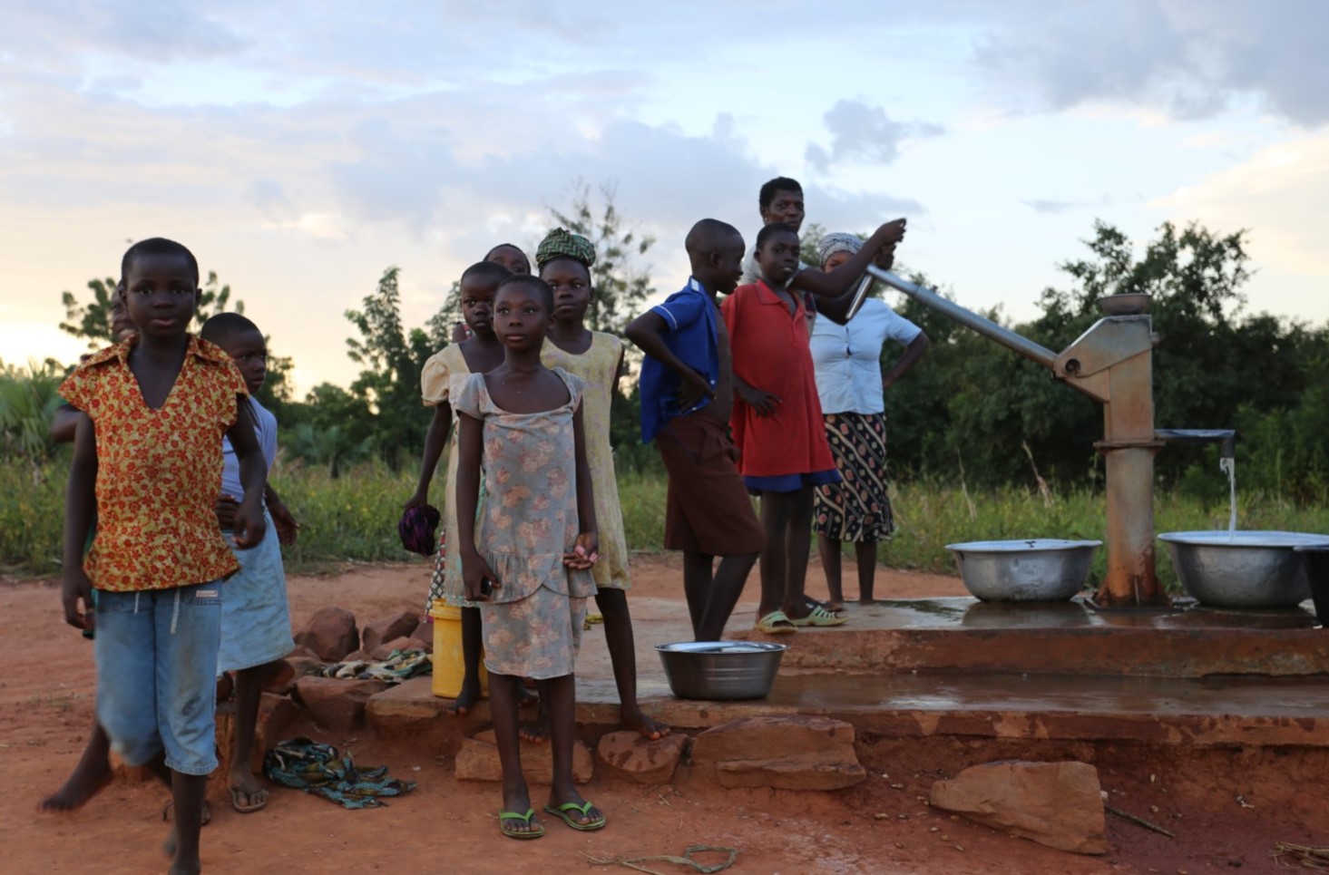 Residents of an African village wait for water at the well pump.