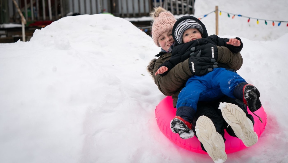 Two kids on a plastic sled going down a hill.
