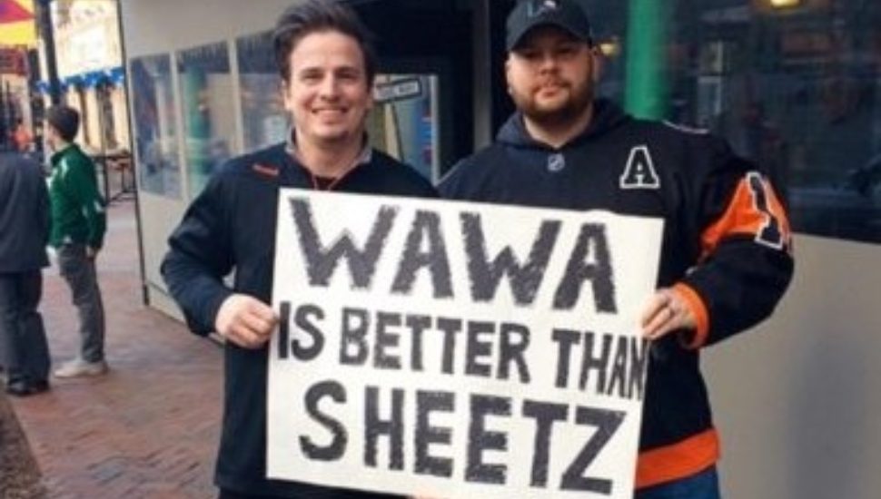 Convenience stores battle it out. Two men hold a Wawa is Better than Sheetz sign