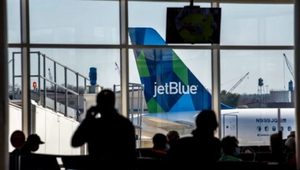 A JetBlue airplane is parked outside at the Philadelphia International Airport while people inside the terminal wait for their flight