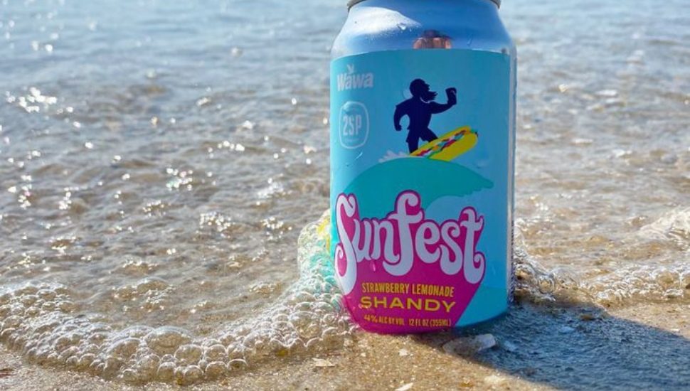 A can of Sunfest Strawberry Lemonade Shandy placed on the sand by the ocean.