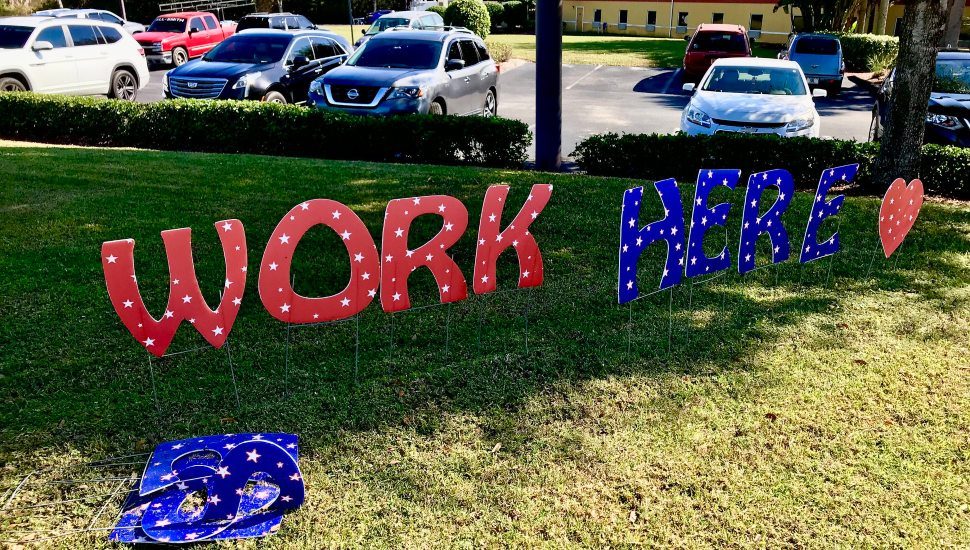 A "Work Here" sign on a lawn.