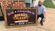 Semo poses with a Rocko Pizza sign outside his shop in Woodlyn.