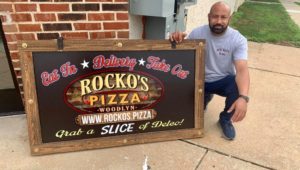Semo poses with a Rocko Pizza sign outside his shop in Woodlyn.