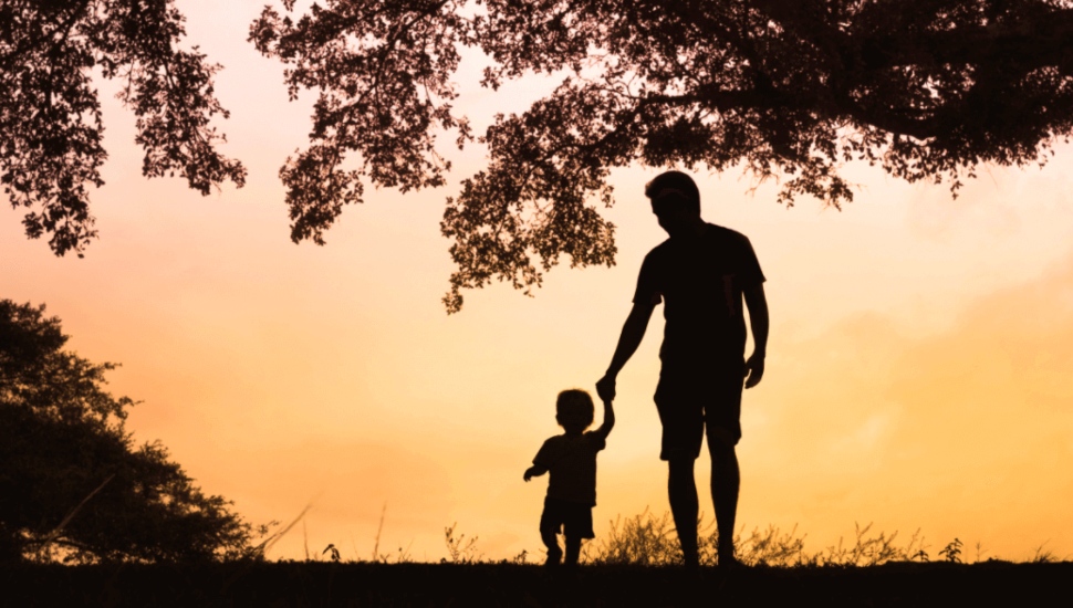 A father hold his child's hand outside.