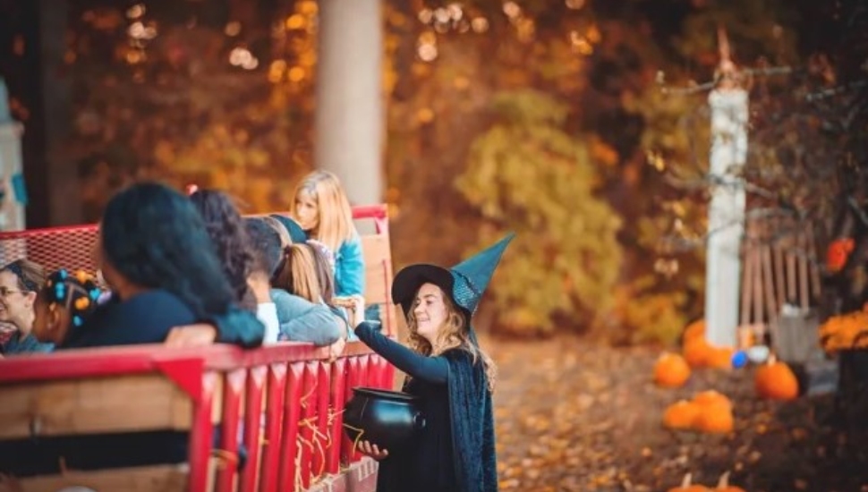 A woman dressed as a witch talks with kids on a hayride.