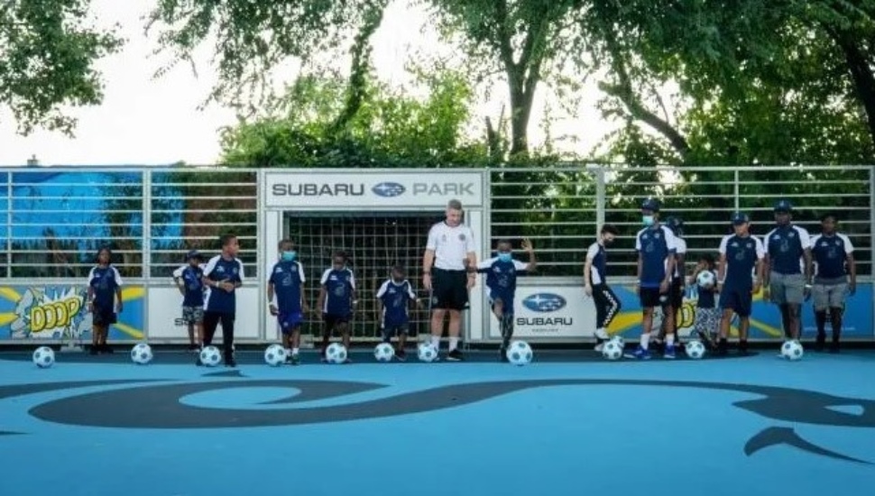 Soccer Coach Phil Griffiths and several children kick soccer ball at a new Mini-Pitch.