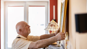An older man hanging a picture