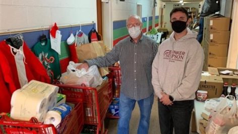 Jeff Hammons with Media Food Bank and a staff member of Brinker Simpson standing with some of the collected food and other items in the food drive.