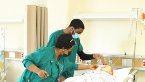 A man and a woman in medical garb looking at a simulated patient in a hospital bed.