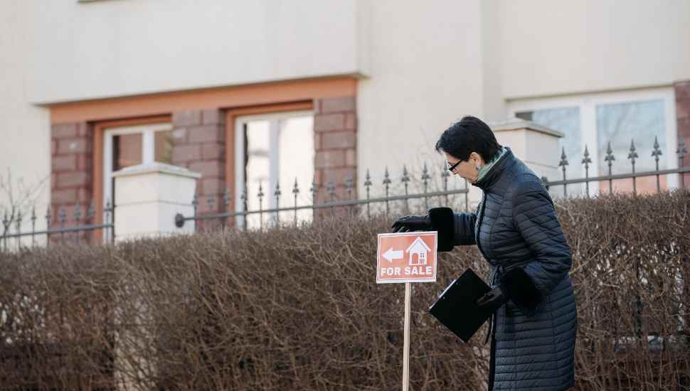 woman puts up a house for sale sign. Housing market looks good for sellers in 2022.