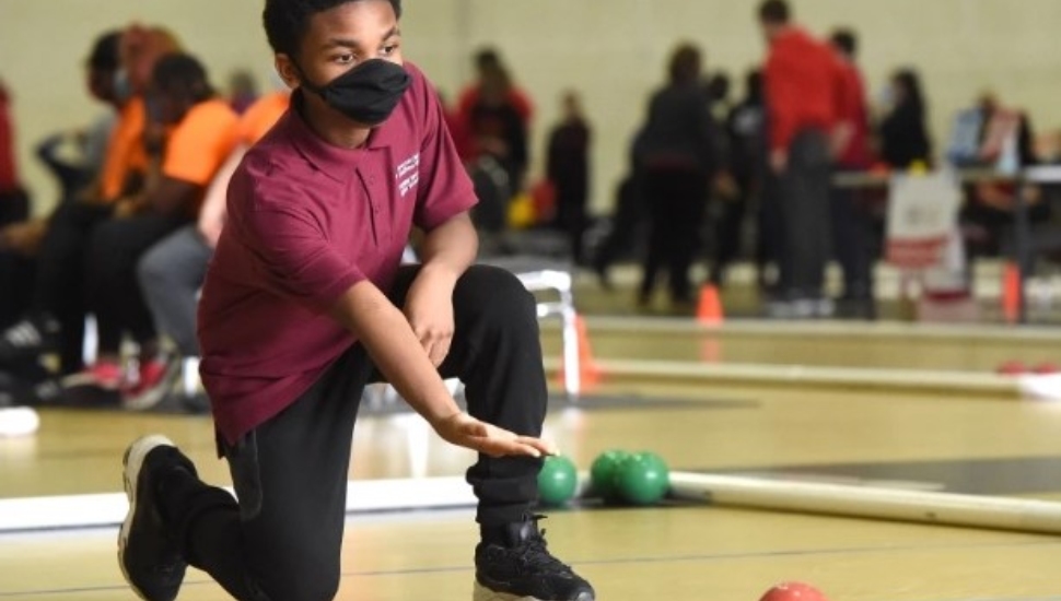 A high school student rolls a bocce ball.