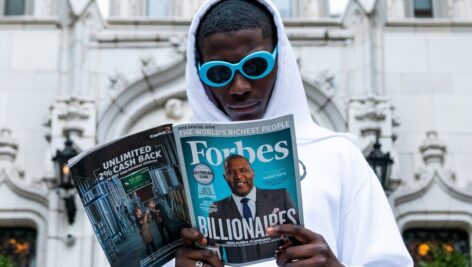 Man outside reading a Forbes Magazine with the Billionaires story as the cover.