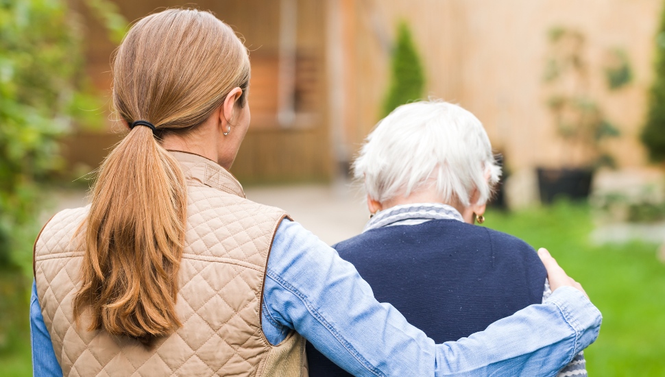 A woman guiding an elderly Alzheimer's patient on an outdoor walk.