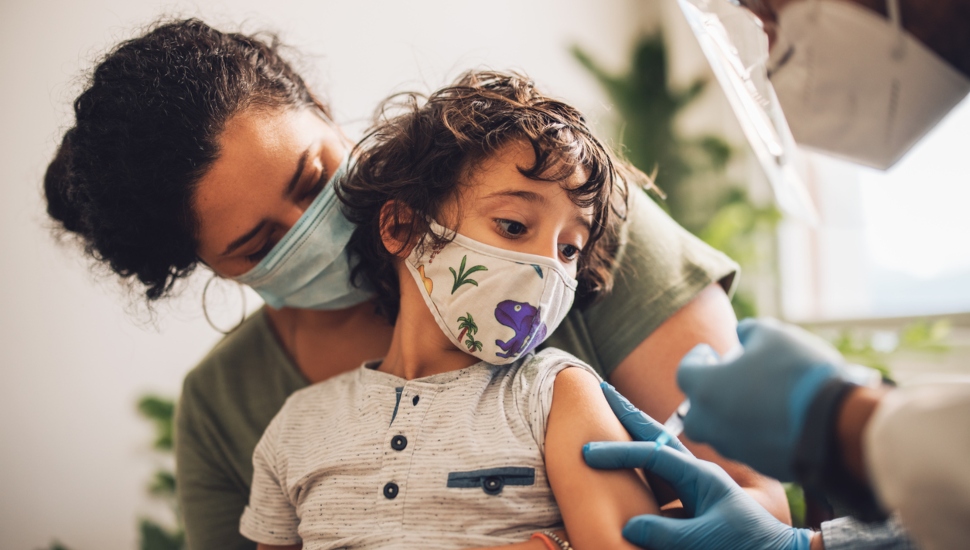 A child with his mother receiving a COVID-19 vaccine from a health care worker.