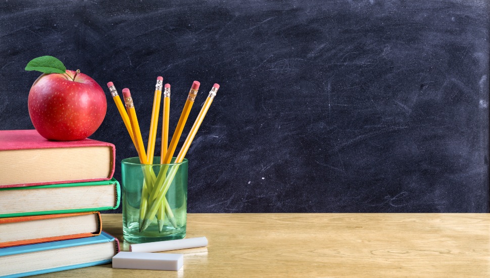 An apple on top of books and a cup of pencils on a teacher's desk.