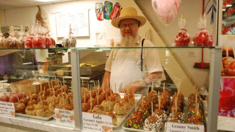 An Amish clerk behind a counter of caramel apple at Booth's Corner Farmers Market.