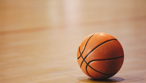 A lone basketball resting on the floor of an indoor basketball court.