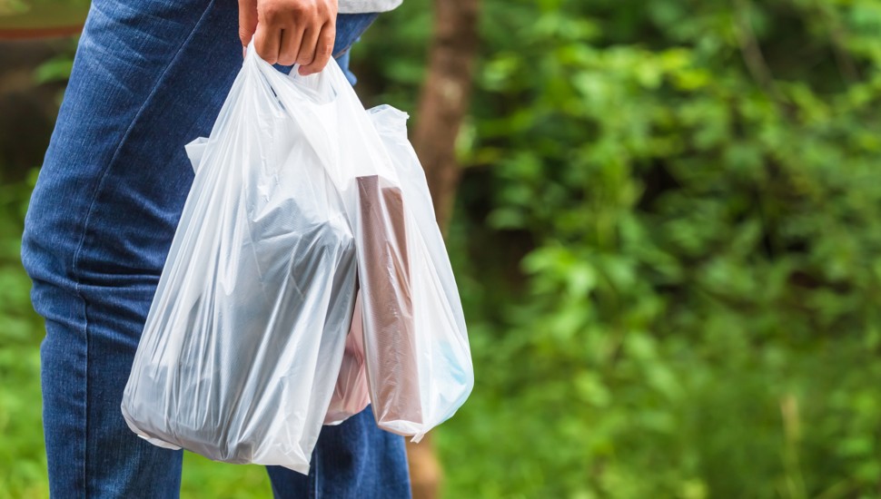 A woman walking in a park carrying a plastic shopping bag