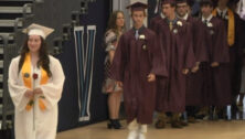 A high school girl in a graduation gown leading a procession of graduates.