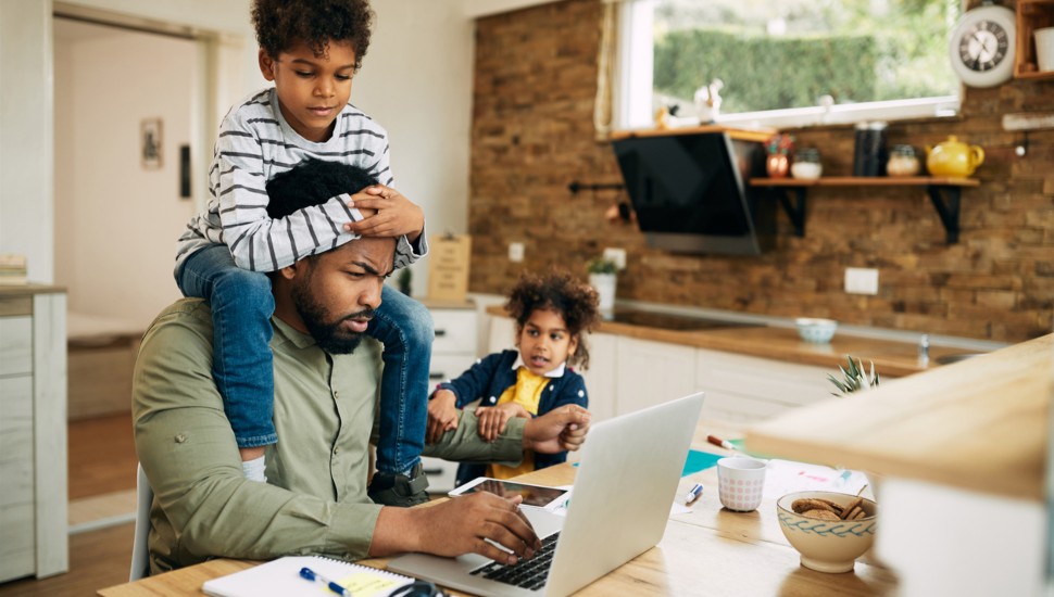 A pandemic lifestyle--man works from home on his laptop distracted by his 2 children.