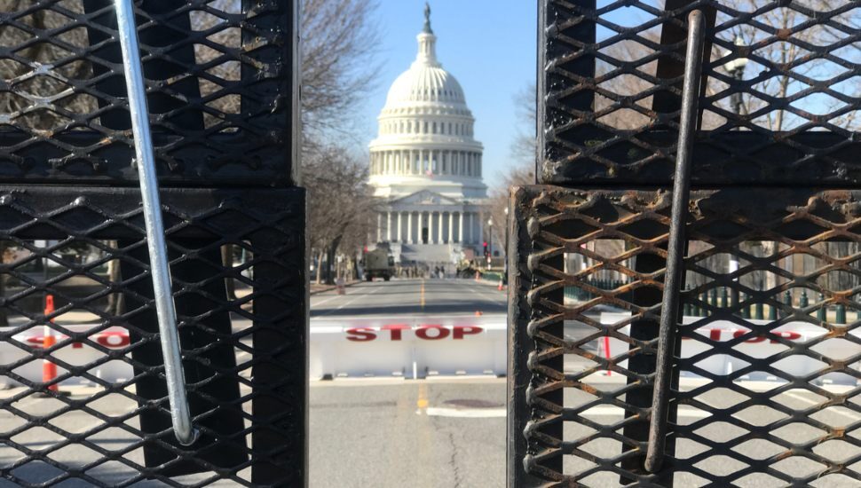 The U.S. Capitol in the distance with an iron gate and a barricade that says 'stop' in the foreground