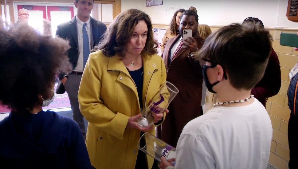 Cindy Marten visiting elementary school, holding two cups and talking to student wearing mask