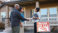 Couple shakes hands with realtor in front of their new home