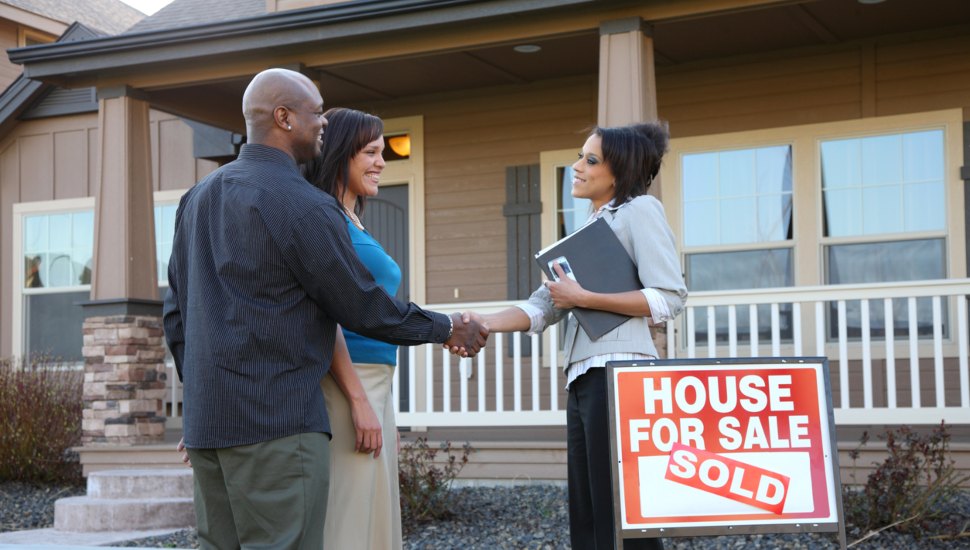 Couple shakes hands with realtor in front of their new home