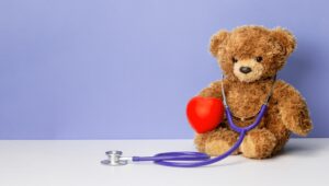Teddy bear with a stethoscope and a heart on a purple background. Family doctor or pediatrician concept. Template Copy space for text.