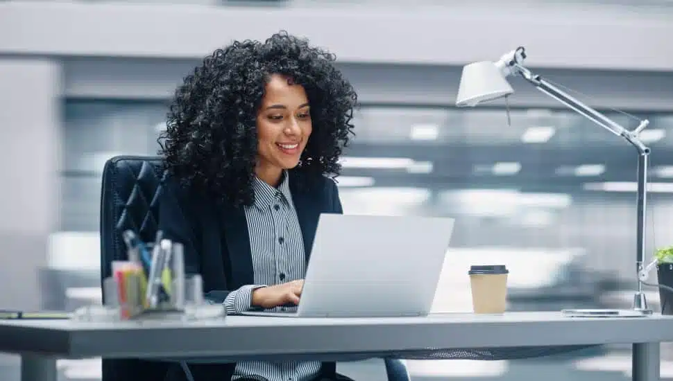 Modern Office: Businesswoman Sitting at Her Desk Working on a Laptop Computer.