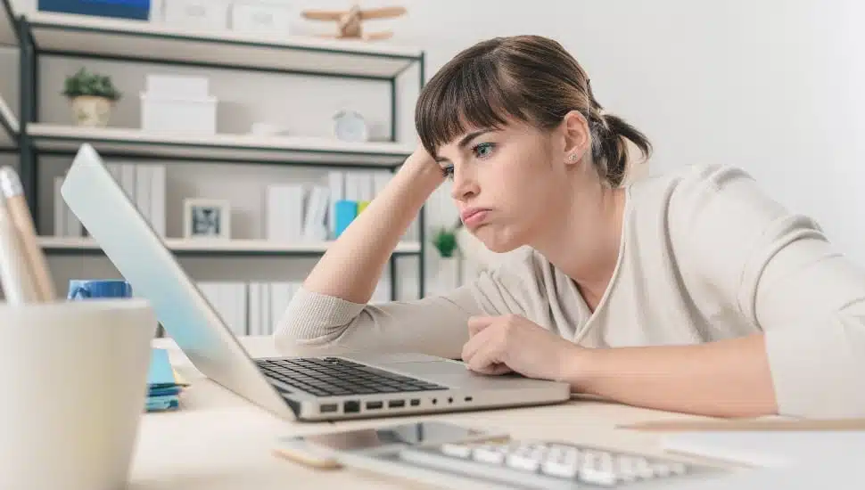 Tired disappointed woman working at office desk with a laptop, connection and computer problems concept