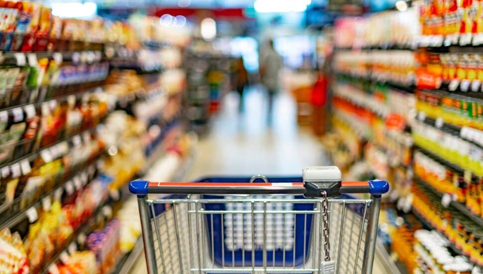An empty grocery cart in the aisle surrounded by supermarket shelves and products