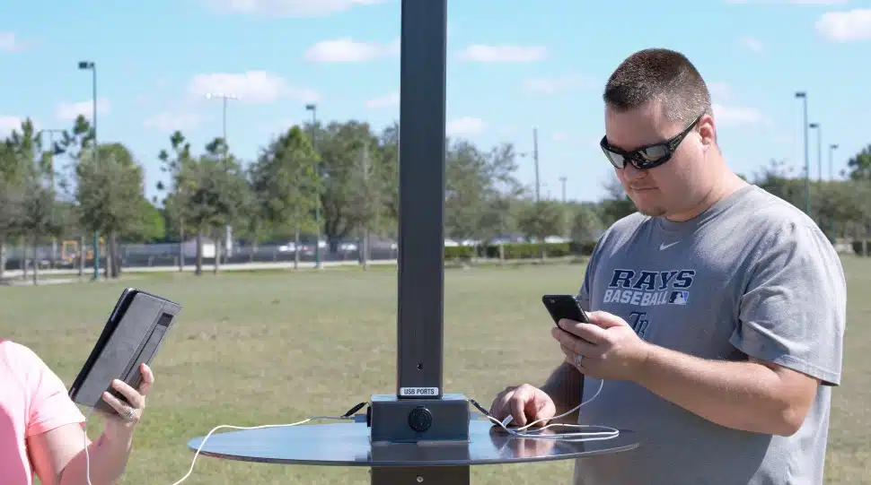 Two men charging their smartphones at an outdoor solar charging station